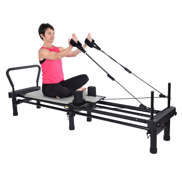 Woman seated cross feet on pilates while pulling the handstraps.